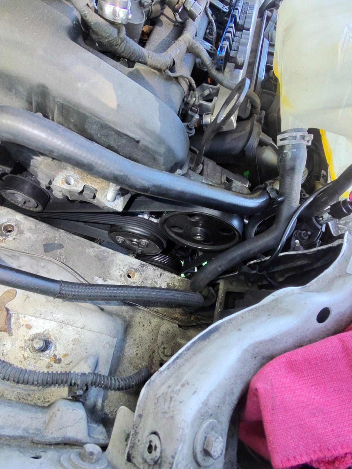 Engine bay with serpentine belt routed around pulleys and a rag resting on the fender