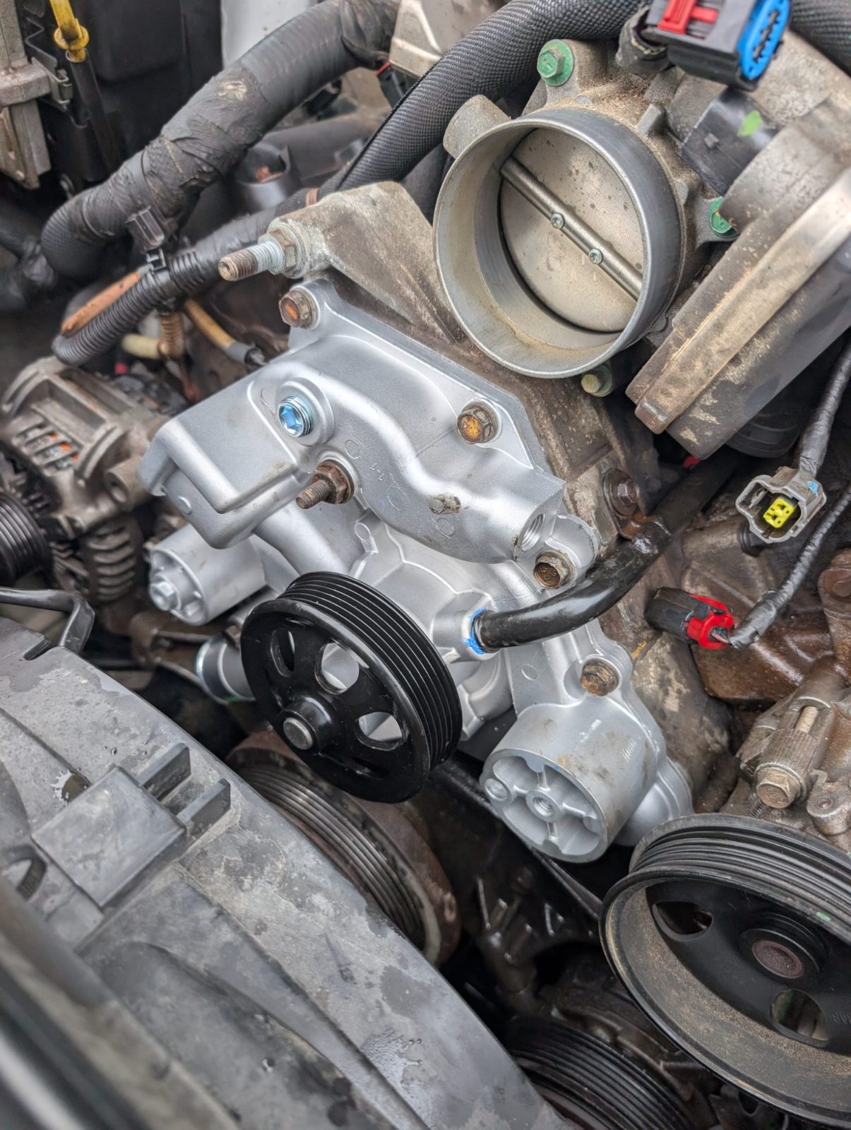 Newly installed water pump and pulley in an engine bay beside the throttle body