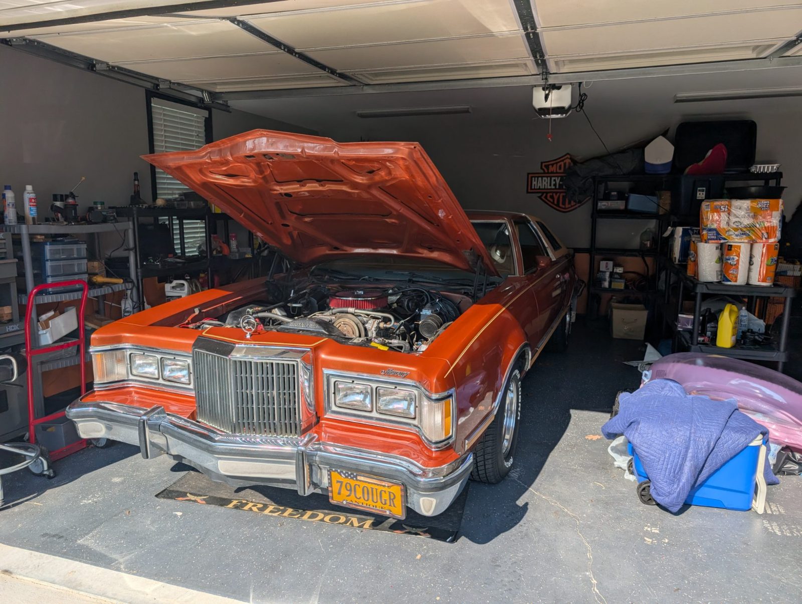 Orange classic coupe parked in a garage with the hood raised over the engine
