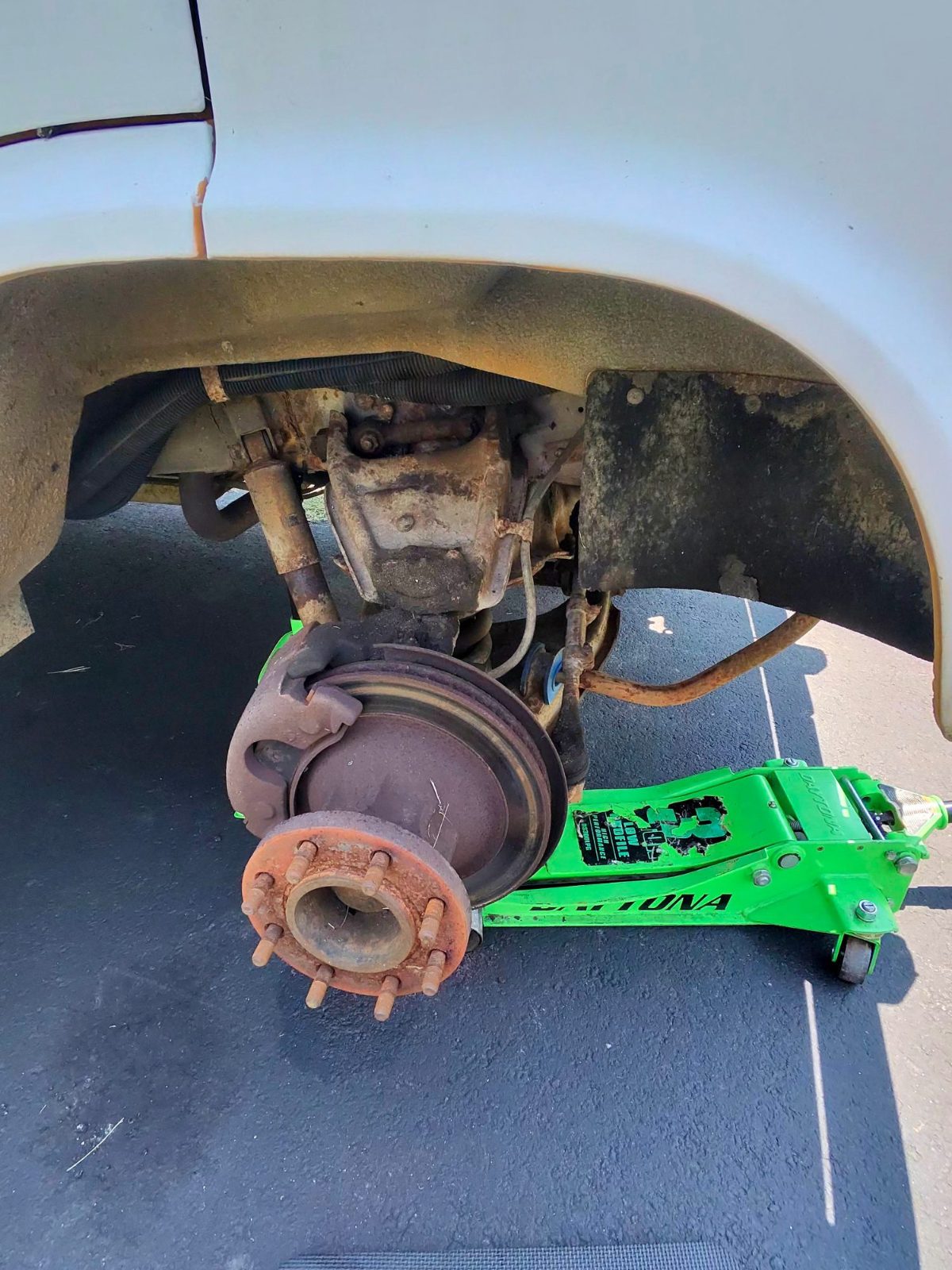 Rear wheel off a white truck with brake drum exposed and a green floor jack alongside